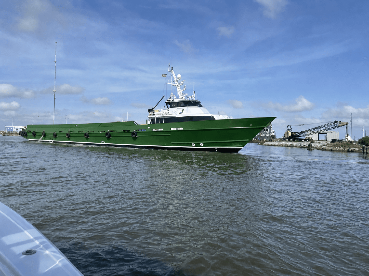 Green and white offshore support vessel underway near a port